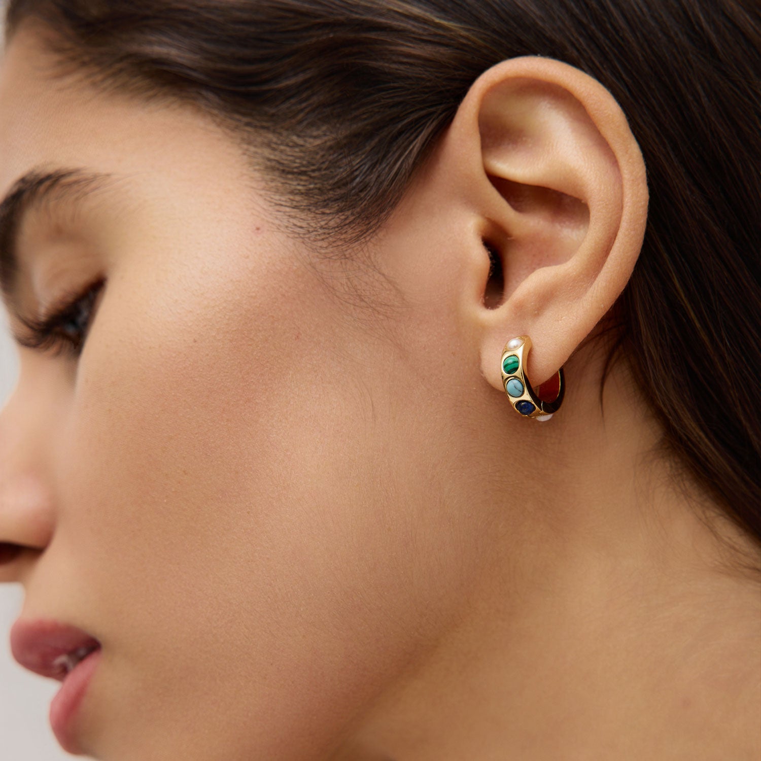 Close-up of a woman's ear wearing a colorful stone hoop earring.