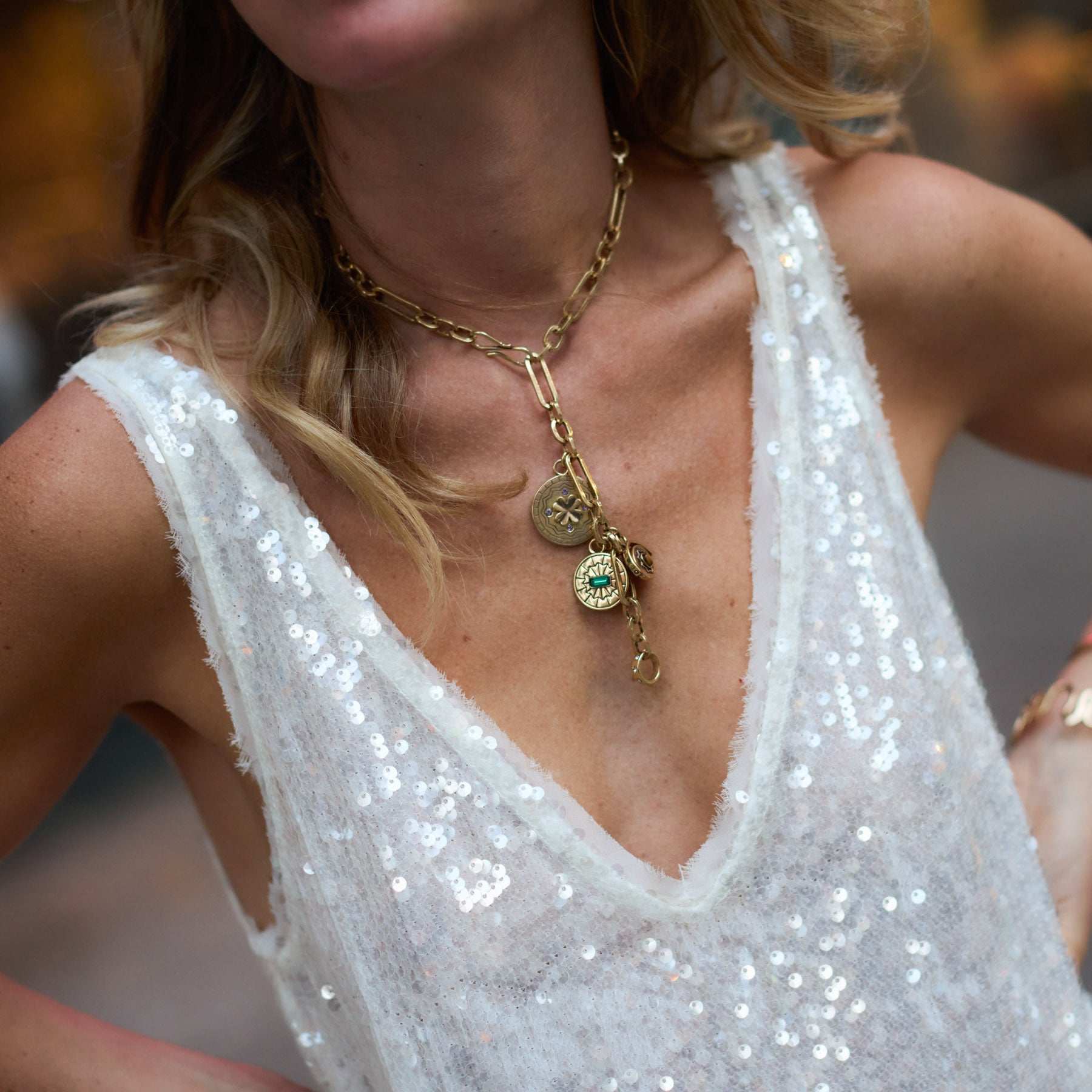 Close-up of a person wearing a gold necklace with charms on a sequined top.