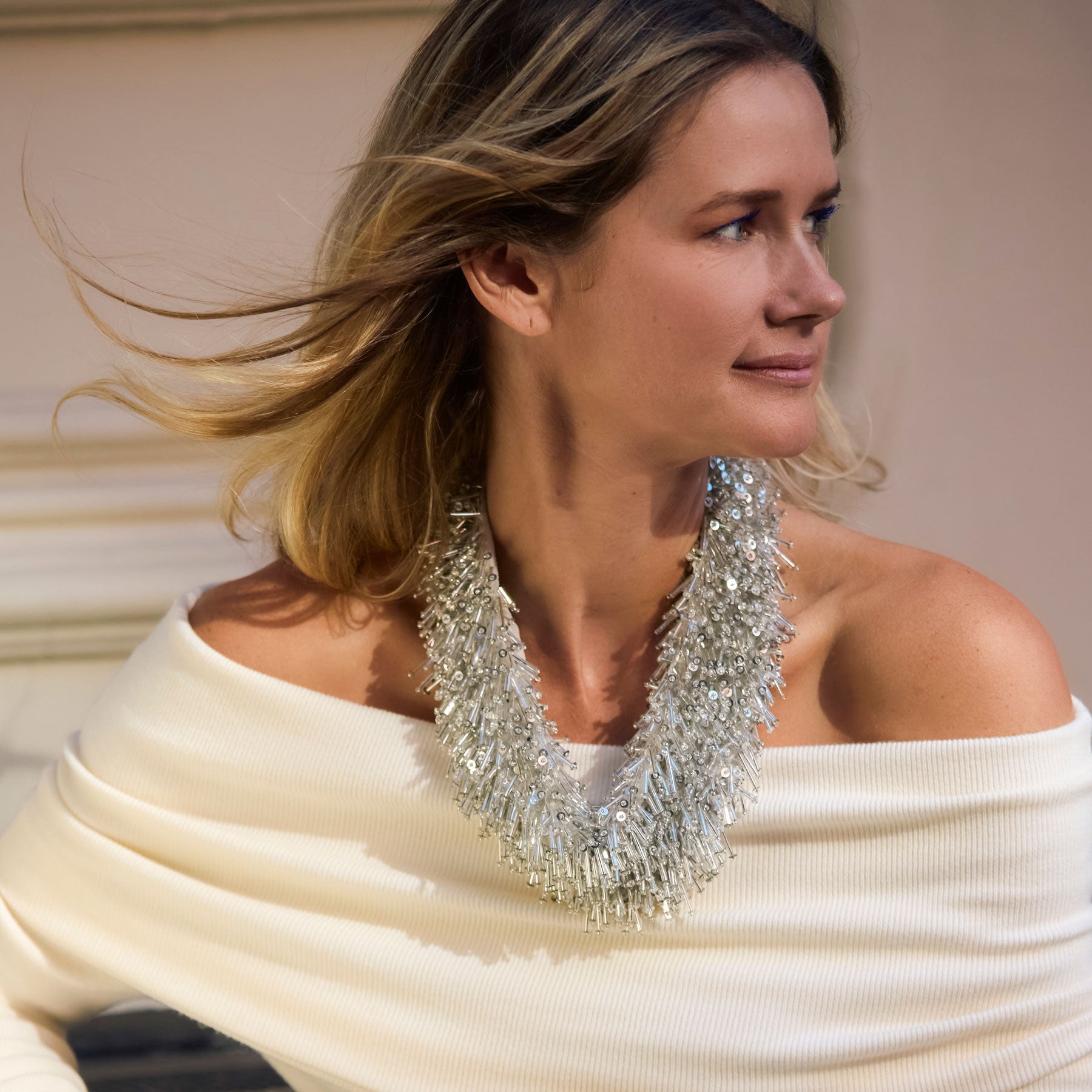 Woman wearing a white off-shoulder top and a sparkling silver beaded scarf necklace against a neutral background