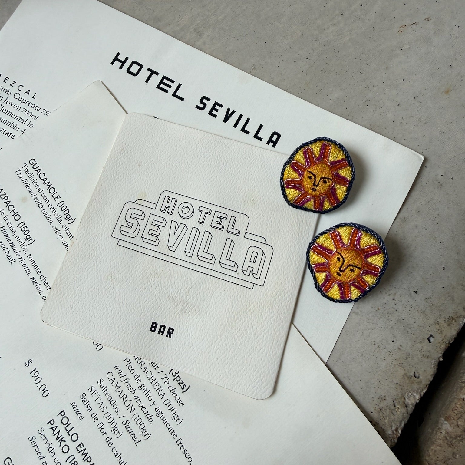 Two sun-shaped earrings on a piece of paper with 'Hotel Sevilla' printed on it.