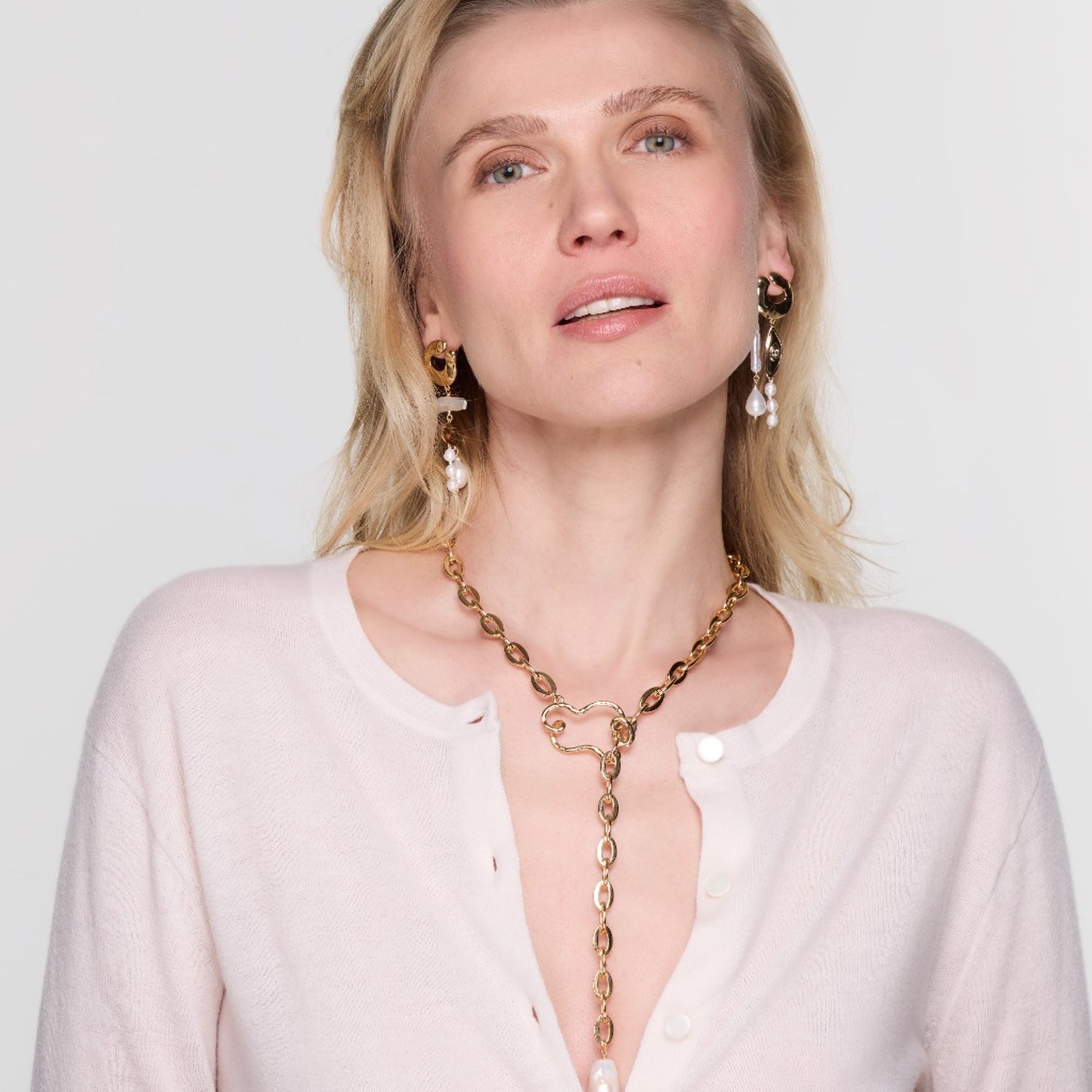 Woman wearing a gold necklace and earrings on a plain background