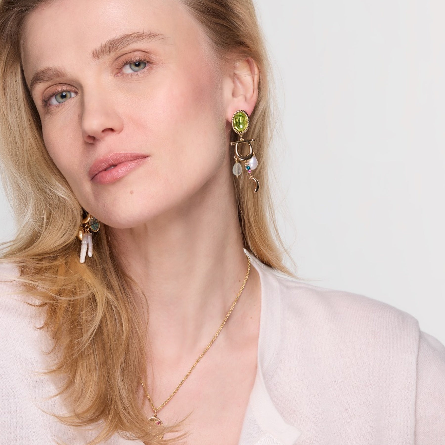 Woman wearing gold earrings with green gemstones on a white background
