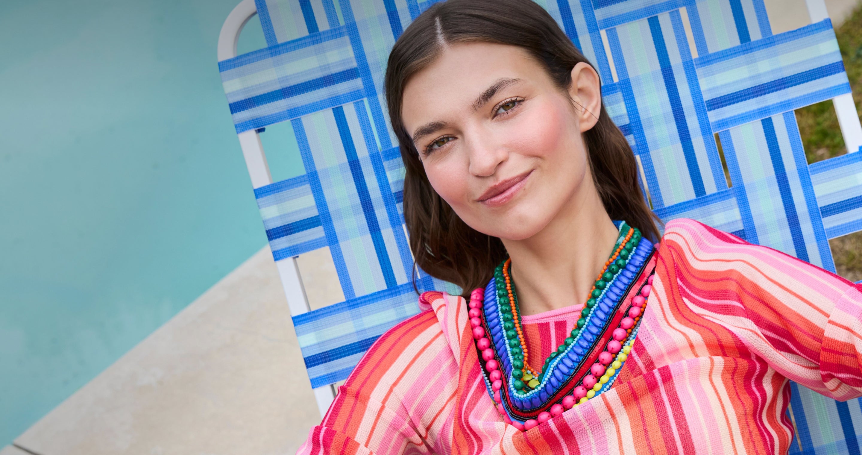 Woman wearing a colorful striped shirt and necklace in front of a blue geometric patterned background