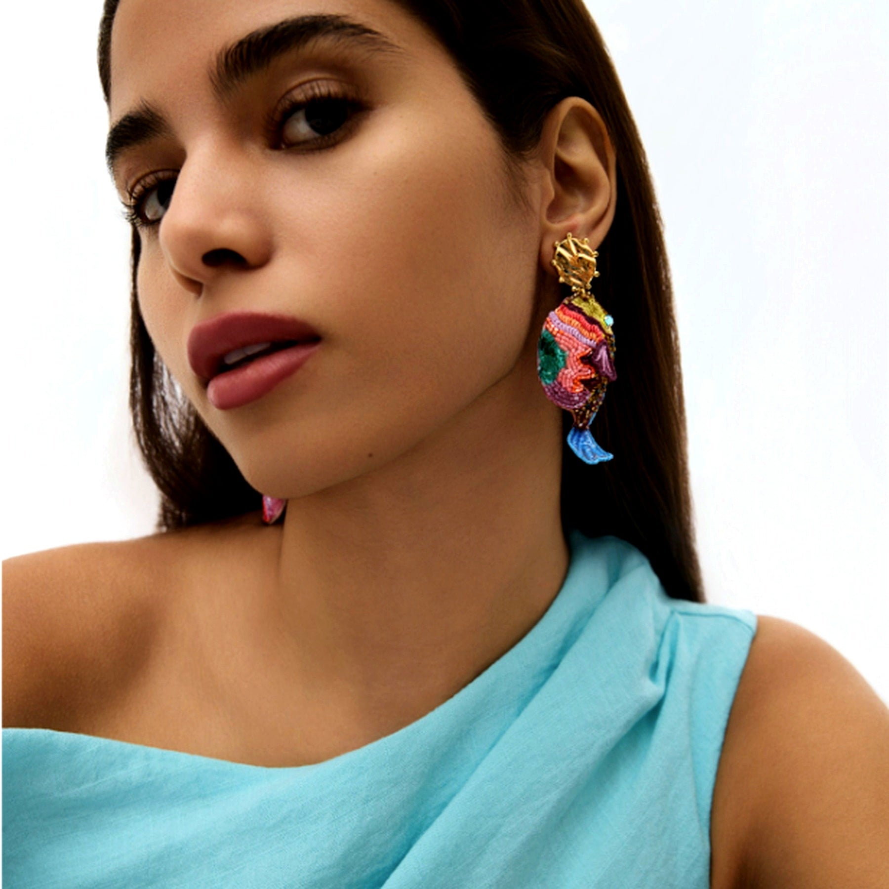 Close-up of a woman wearing colorful earrings with a light blue top against a white background