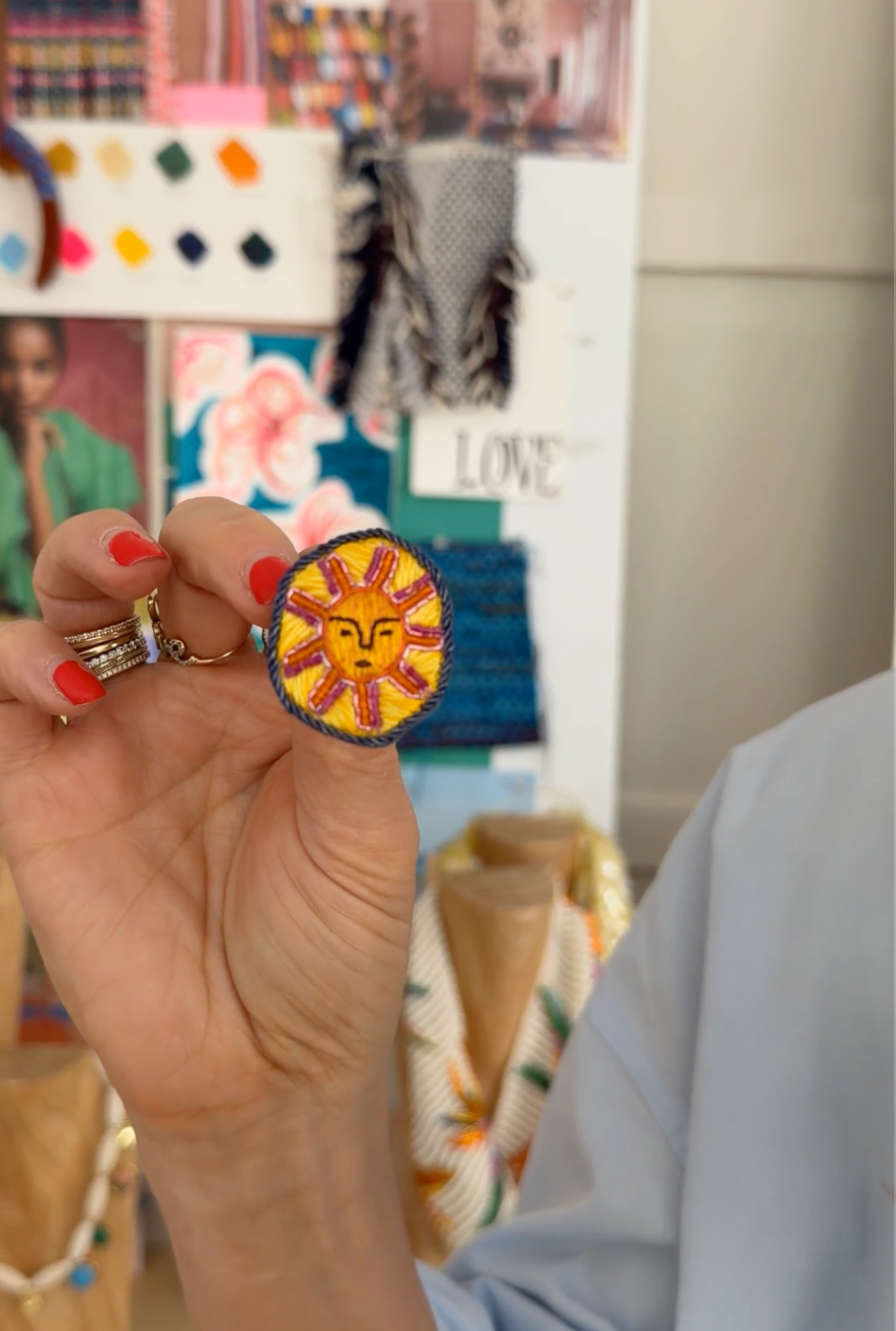 Video of model hold embroidered earring stud with a sun face on the against a mood board background
