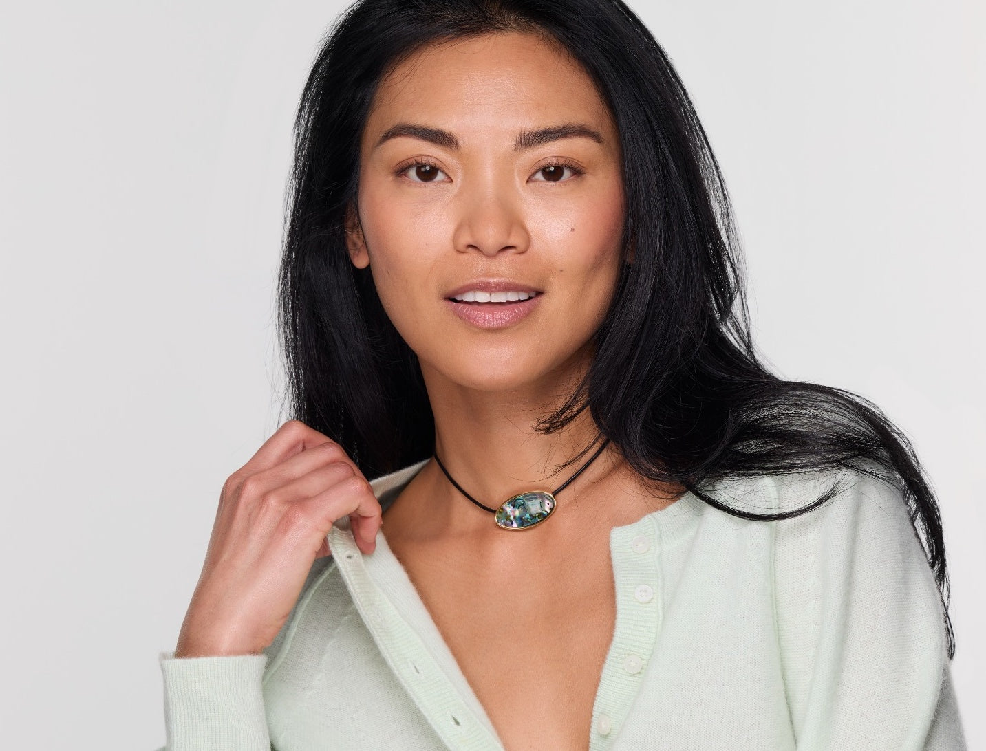Woman wearing a light green shirt and necklace with a white background