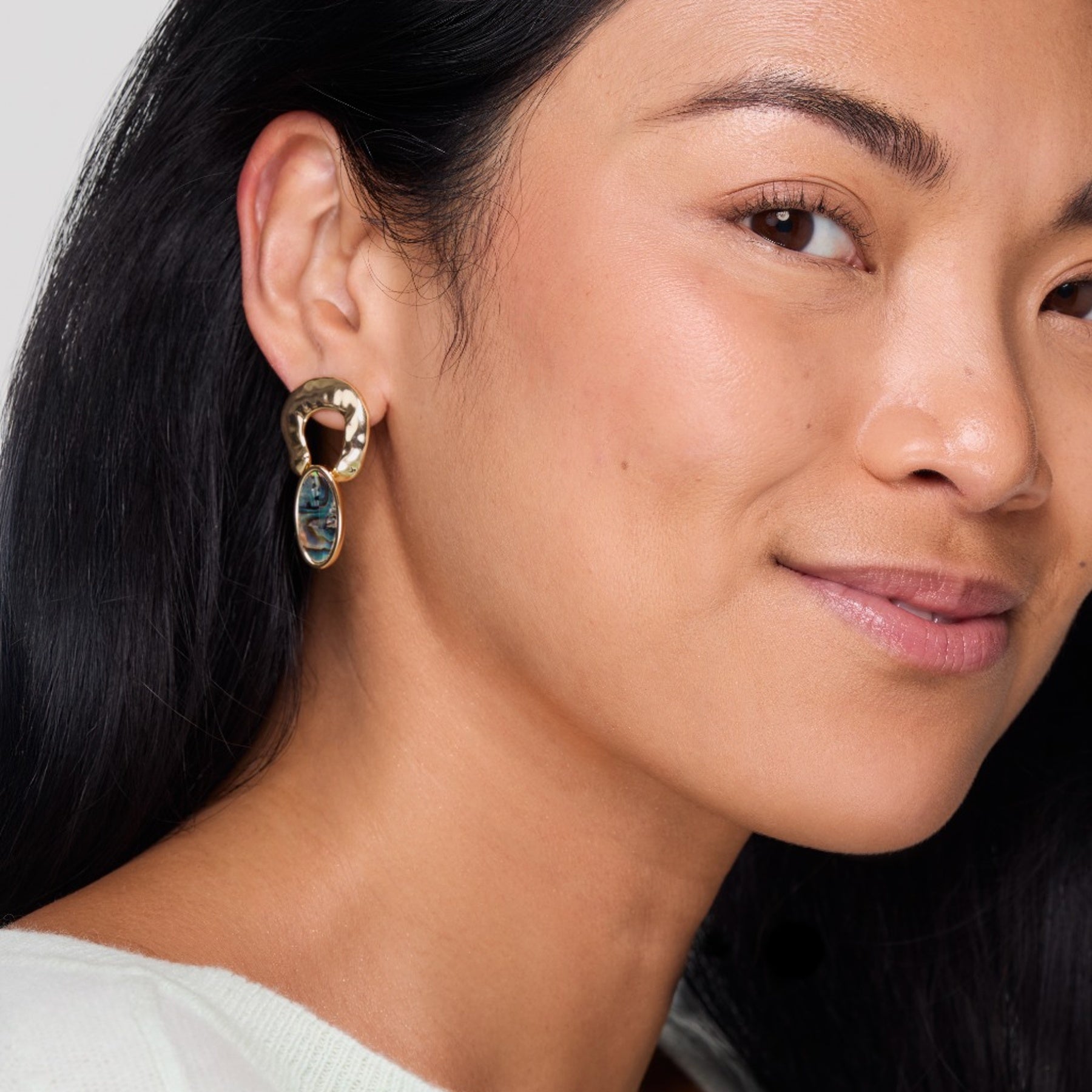 Close-up of a woman wearing a gold earring with a blue gemstone.