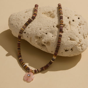 brown bead necklace with pink and crystal flower charm laid on a white porous stone
