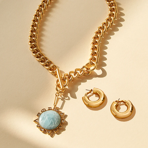 Odyssey gold necklace with blue crystal and Emma gold hoop earrings laying side by side