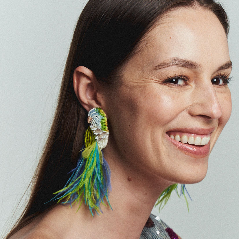 feathered bird earrings colored in blue green and white worn by a smiling woman