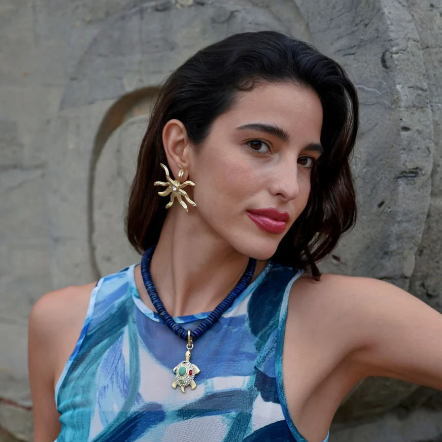 woman posing in profile to show a turtle charm necklace and gold earrings