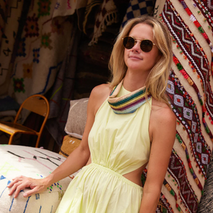 woman wearing a colorful striped scarf necklace, sunglasses, and yellow sleeveless dress