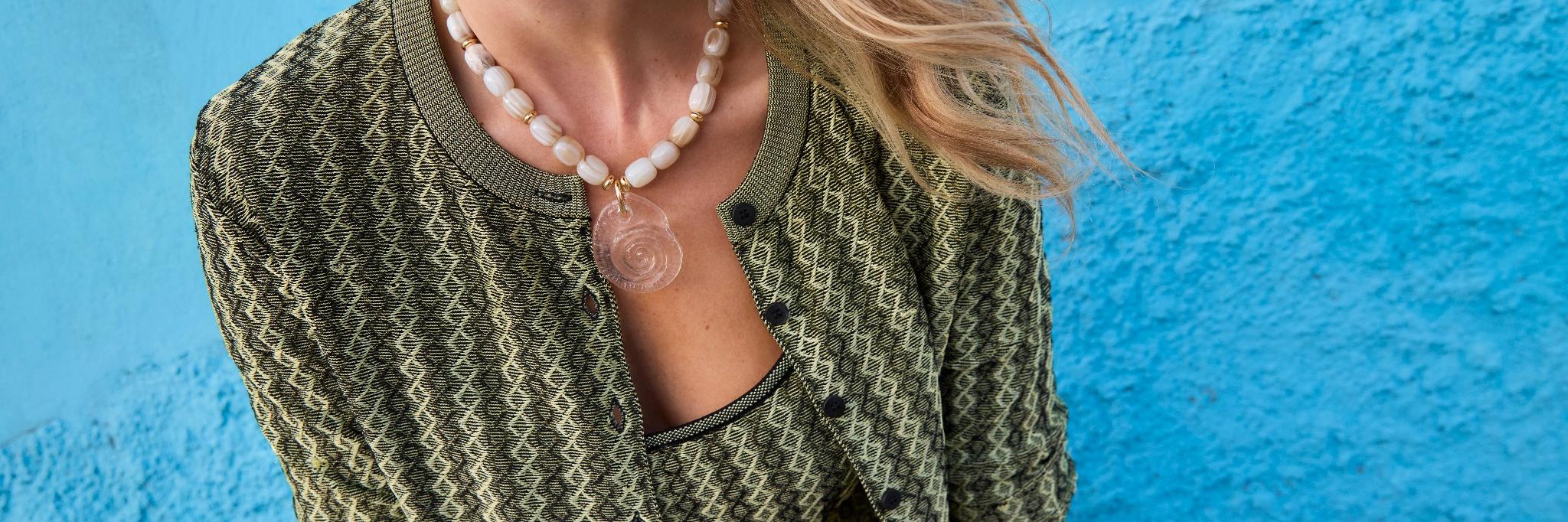 Model wearing a semi precious stone necklace with large clear shell pendant in green sweater against blue background