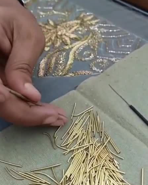 Hand holding a small gold hairpin with a pile of similar hairpins on a textured surface.