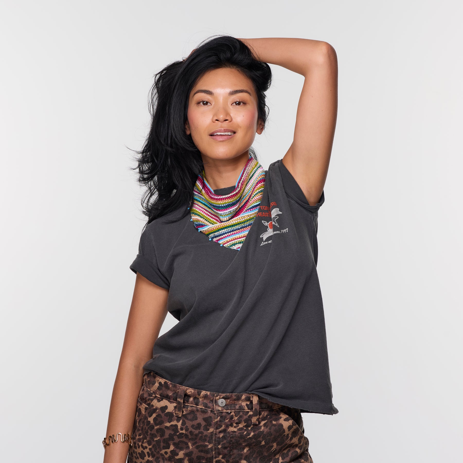 Woman wearing a dark gray t-shirt with a colorful scarf and patterned pants on a light background