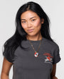 Woman wearing a gold charm necklace on thin chain with grey t shirt on white background