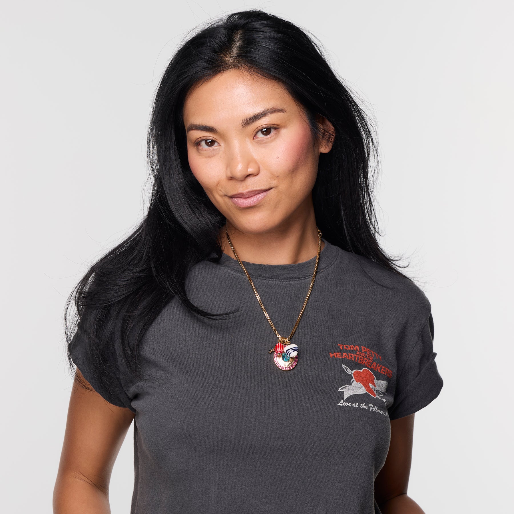 Woman wearing a gold charm necklace on thin chain with grey t shirt on white background