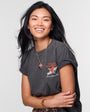 Woman smiling and wearing a gold charm necklace on thin chain with grey t shirt on white background