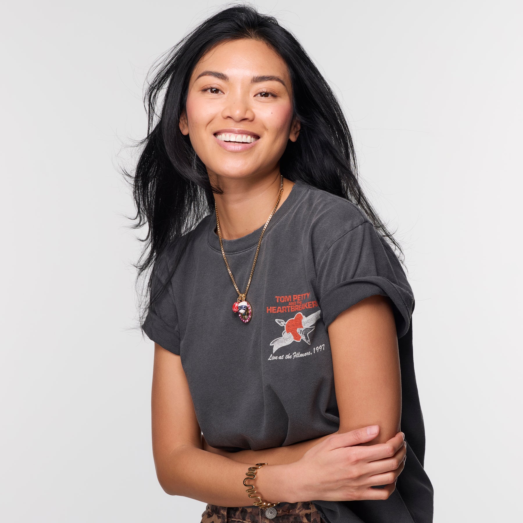 Woman smiling and wearing a gold charm necklace on thin chain with grey t shirt on white background