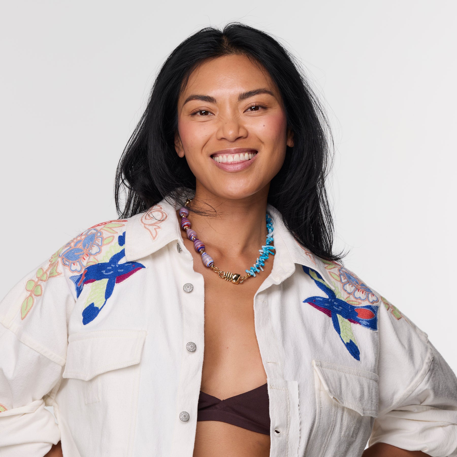 Woman wearing a colorful pink and blue shell necklace against a white background