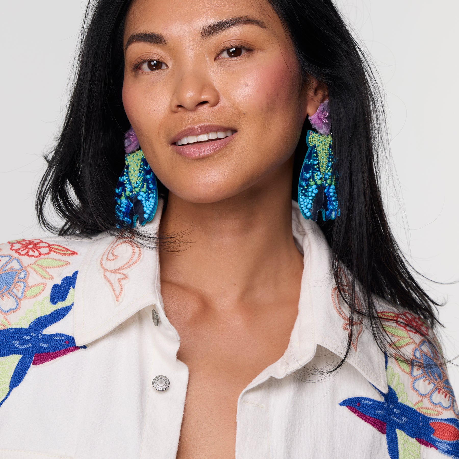 Embroidered colorful earrings on model against white background