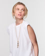 Woman wearing a long gold layering necklace in a white t shirt against a white background