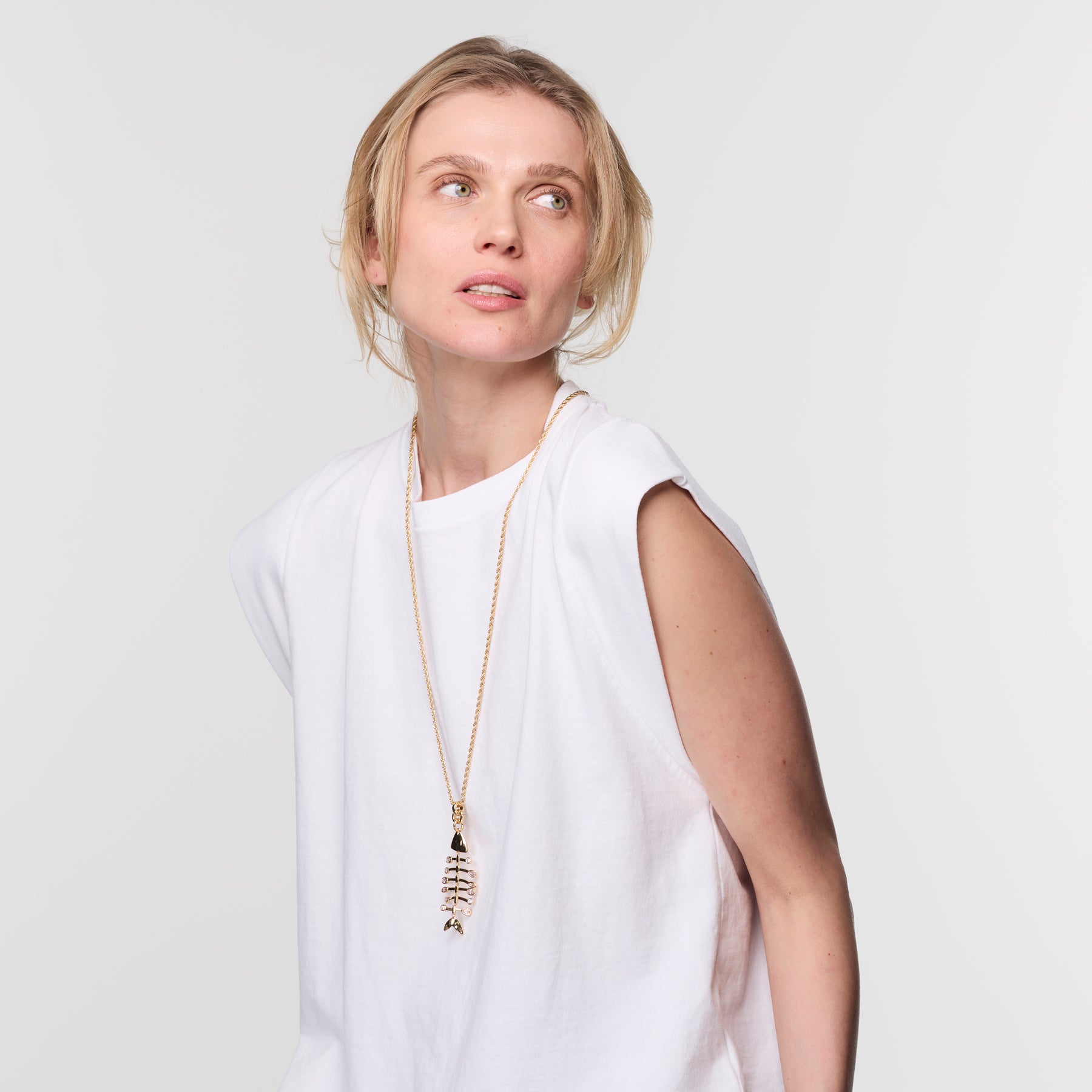 Woman wearing a long gold layering necklace in a white t shirt against a white background