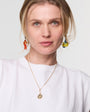 Woman wearing a gold necklace and colorful earrings against a white background