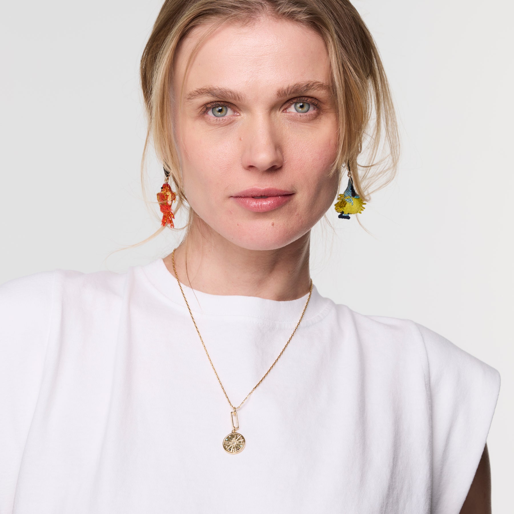 Woman wearing a gold necklace and colorful earrings against a white background
