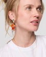 Woman wearing colorful earrings and a white shirt on a light background