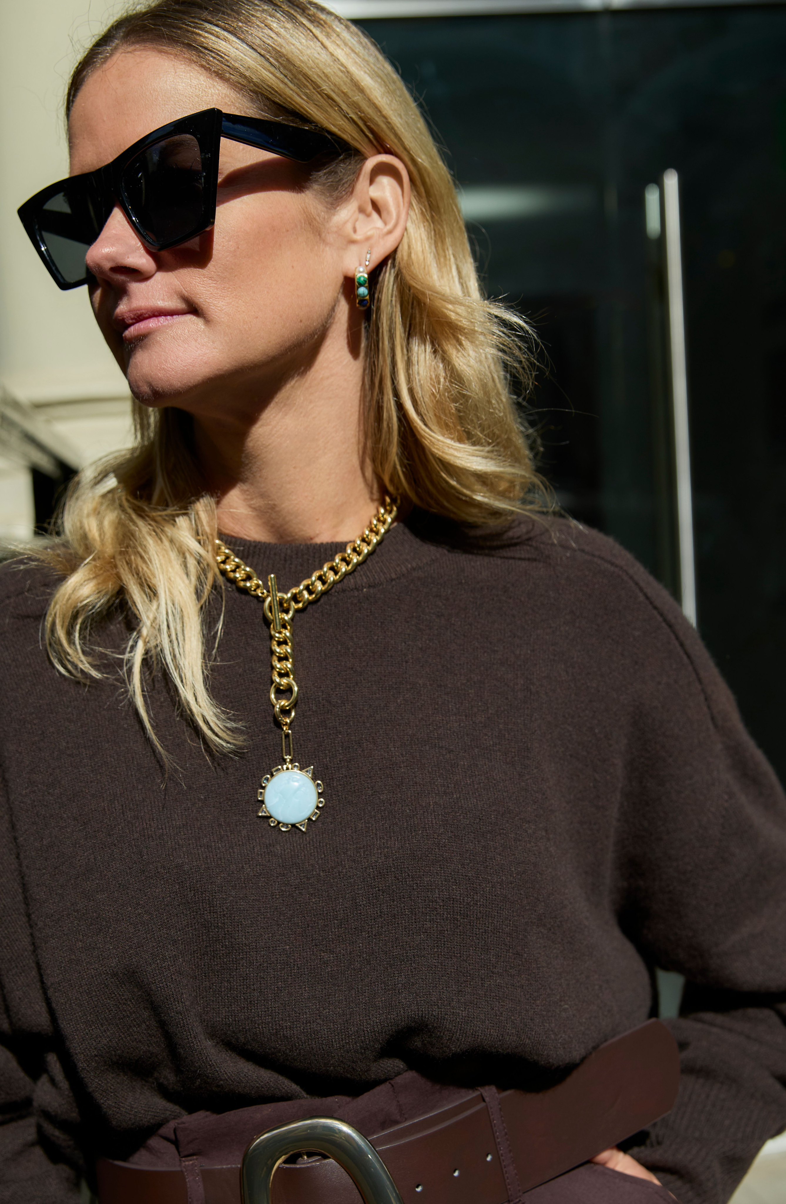 Woman wearing sunglasses and a brown sweater with a gold necklace.