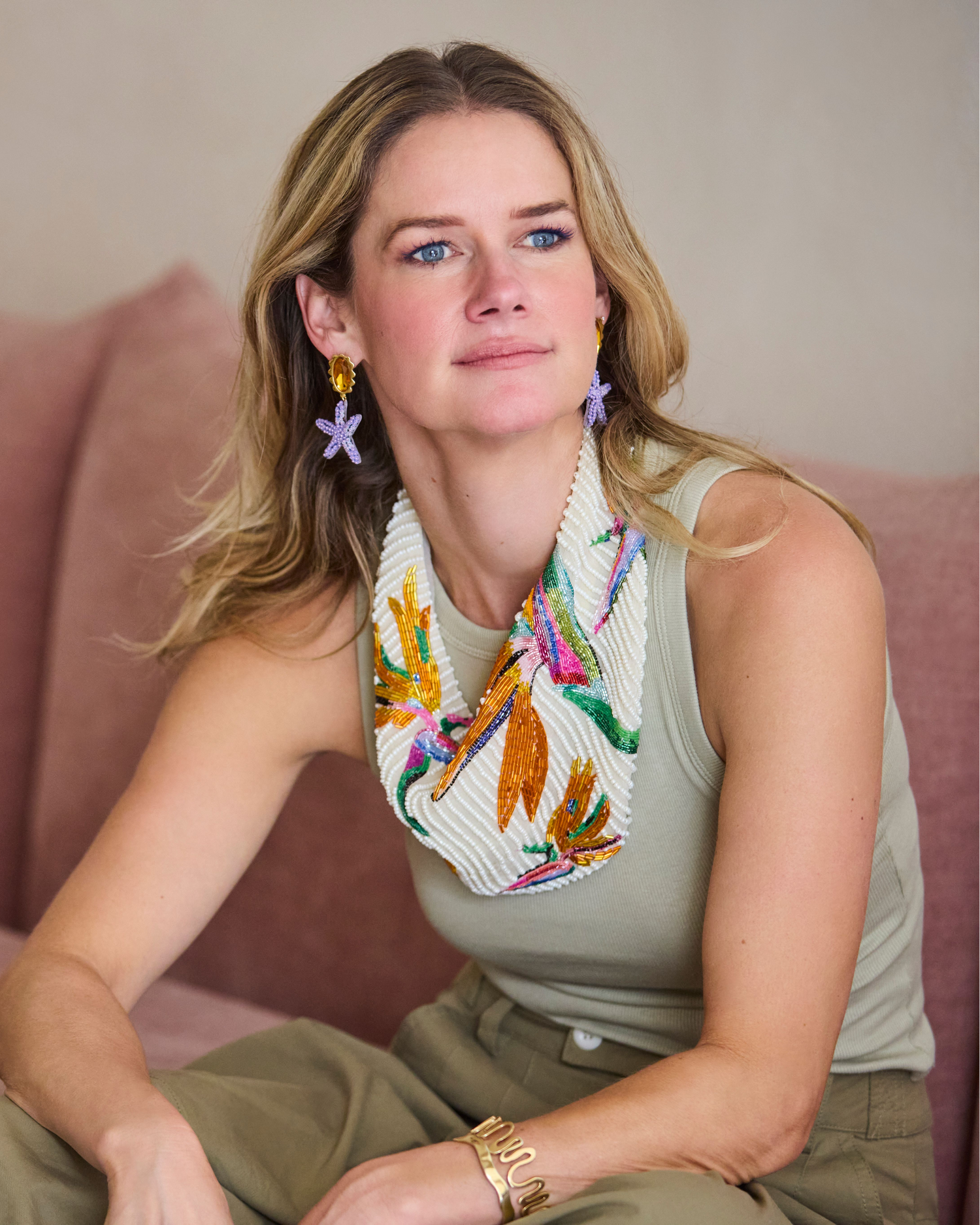 Woman sitting on a pink couch wearing a colorful scarf and earrings.