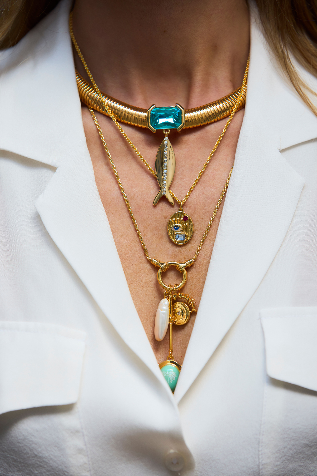 Close-up of a person wearing multiple gold necklaces with gemstones on a white background