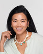 Model wearing gold hoops and white shell charm necklace on white background. 