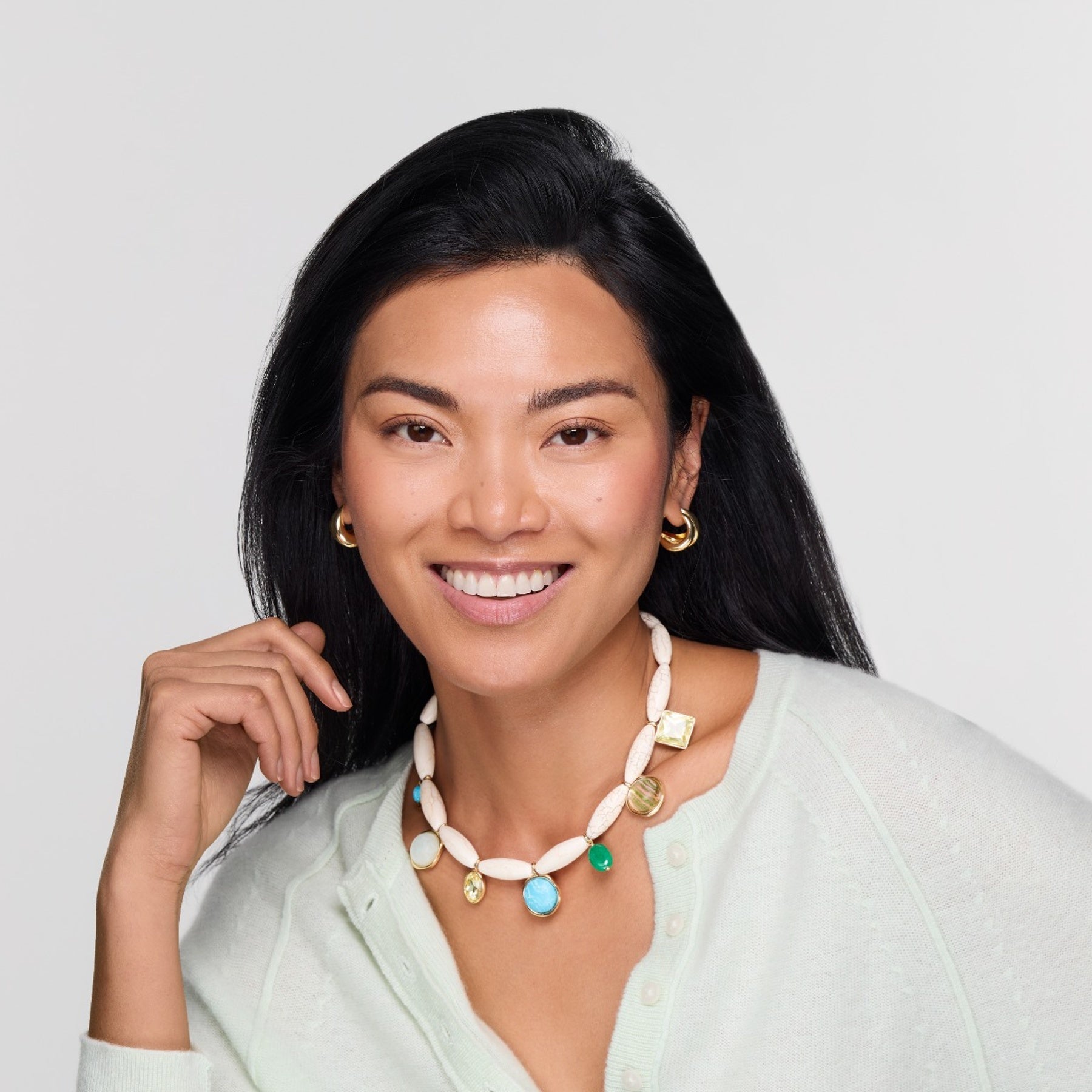 Model wearing gold hoops and white shell charm necklace on white background. 