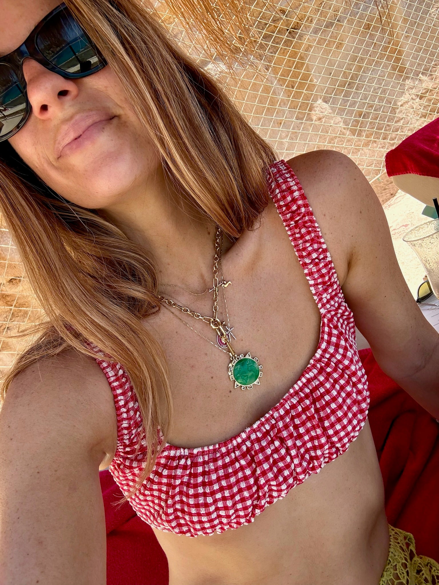 Model wearing a gold chain necklace with a green and gold charm while wearing a red and white checkered bathing suit