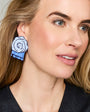 A close-up of a woman wearing a large, geometric, flower-shaped earring in shades of blue, purple, and white.