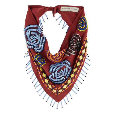 A beaded neck scarf with a deep red base, featuring intricate geometric and floral beadwork in blue, yellow, orange, and black, finished with light blue tassels. The brand label is visible at the collar.