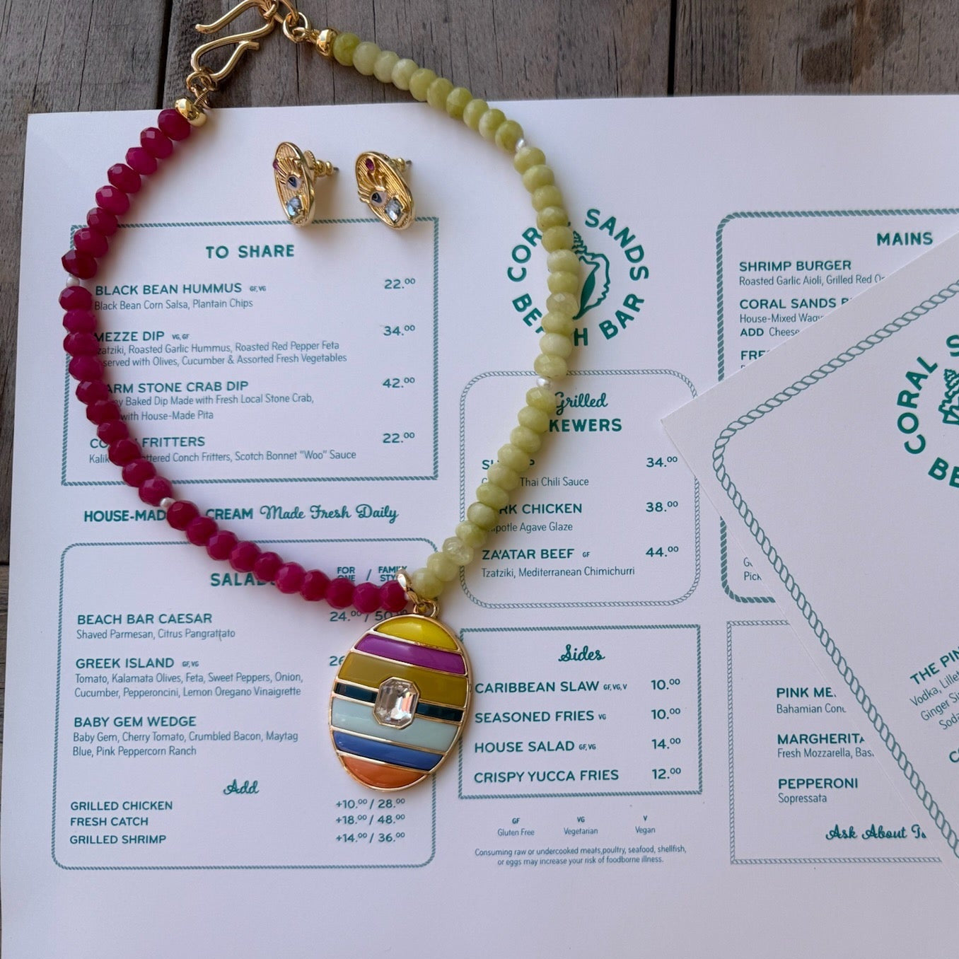 Colorful beaded necklace on a menu with 'Coral Sands Beach Bar' branding.