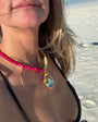 Woman on a beach wearing sunglasses and a necklace with a colorful pendant.