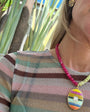Person wearing a colorful striped sweater and beaded necklaces with a decorative pendant outdoors.