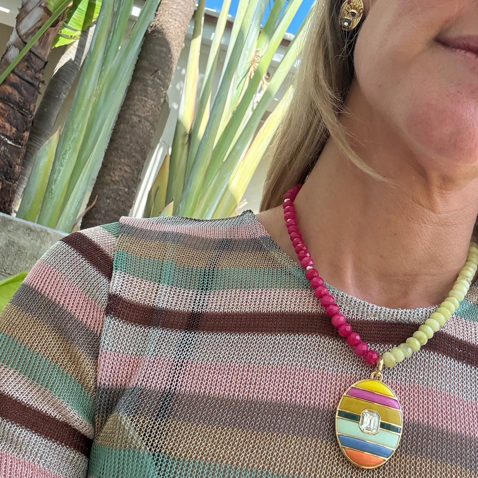 Person wearing a colorful striped sweater and beaded necklaces with a decorative pendant outdoors.