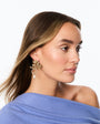 A woman in profile wearing a gold-toned floral hoop earring with a dangling pearl, against a clean white background.