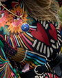 A close-up lifestyle shot of a person wearing a gold-toned snake chain necklace with a round blue stone pendant featuring a gold star. The person is wearing a black blouse with a vibrant, multicolored floral and abstract pattern, paired with a black belt.
