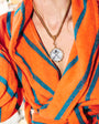 A close-up of a person wearing an orange and blue striped terrycloth robe, accessorized with a gold-tone chain necklace featuring a round pendant with a cross design.