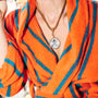 A close-up of a person wearing an orange and blue striped terrycloth robe, accessorized with a gold-tone chain necklace featuring a round pendant with a cross design.