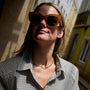 A woman wearirng a green and brown colored tennis necklace in a plaid shirt  against a city landscape