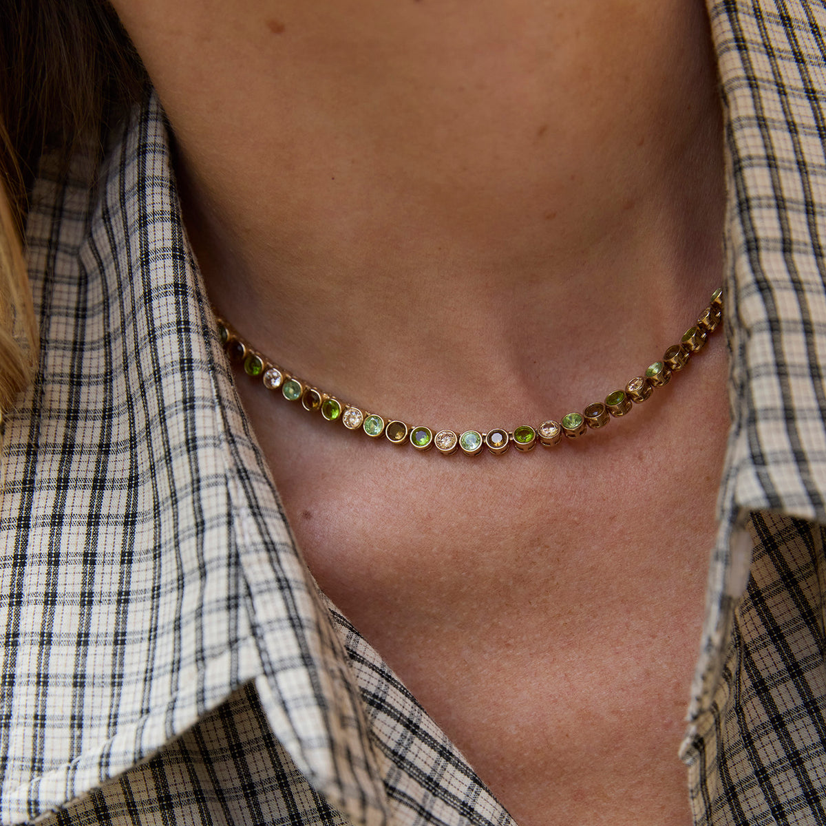 A woman wearirng a green and brown colored tennis necklace in a plaid shirt