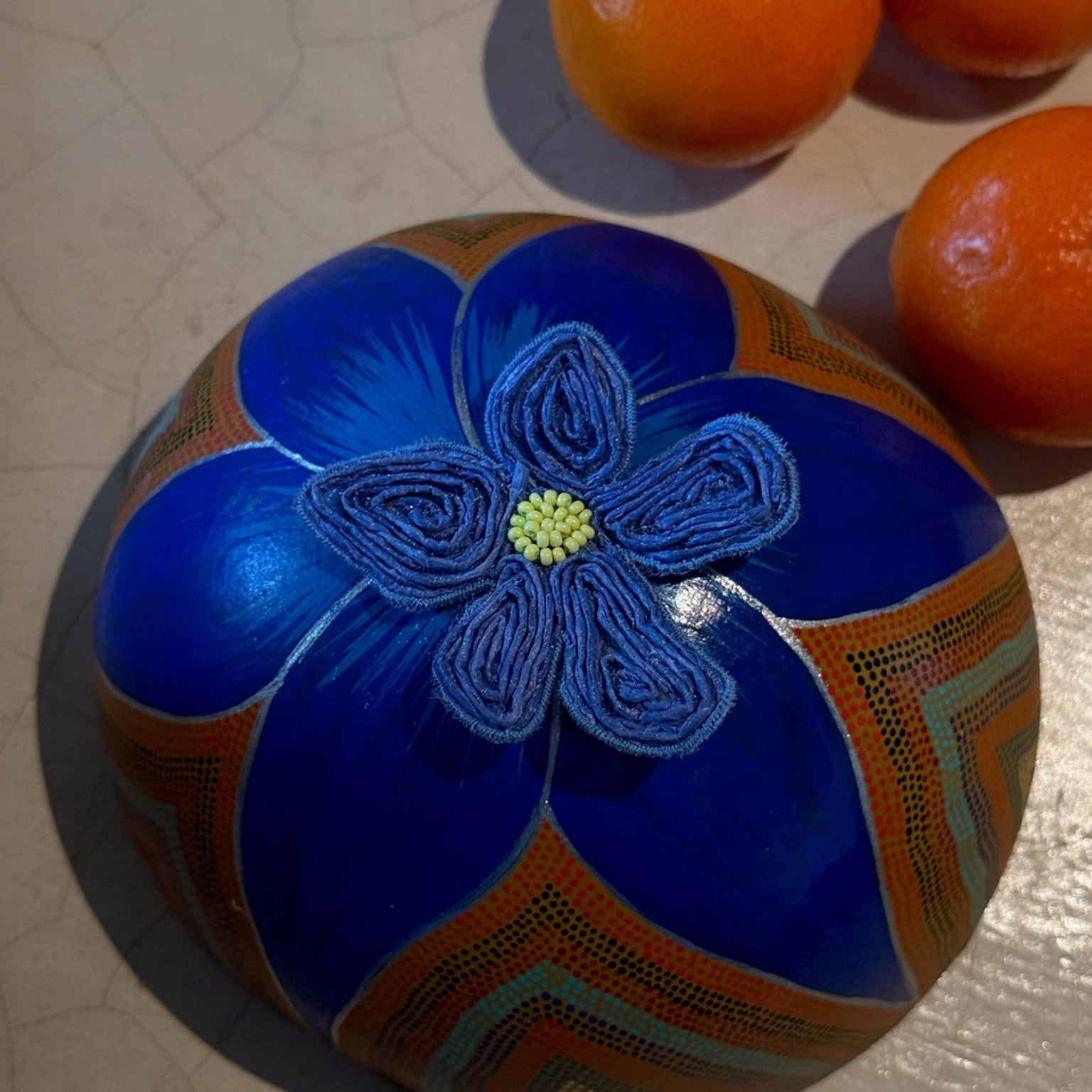 Decorative blue ball with a floral design on a light surface with oranges.