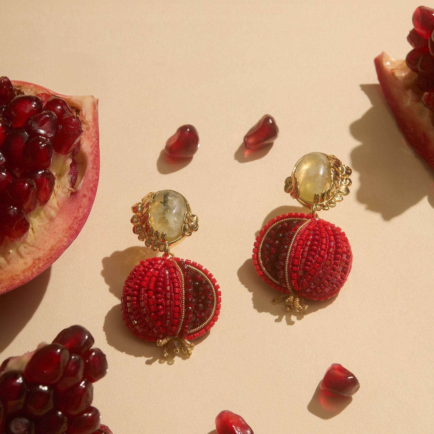 Pomegranate Beaded Double Drop Earrings Staged on Tan Background with Pomegranate Seeds